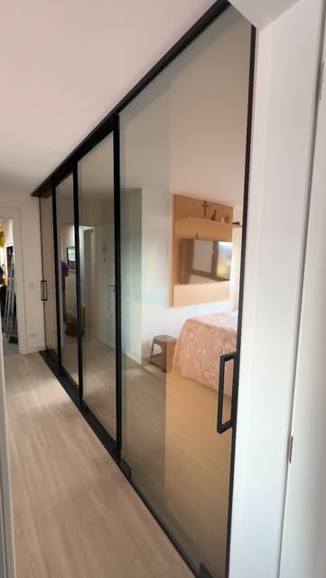 Portas de correr de vidro com moldura preta dividindo corredor e quarto